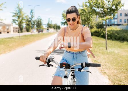 donna con orologio intelligente in bicicletta in città Foto Stock