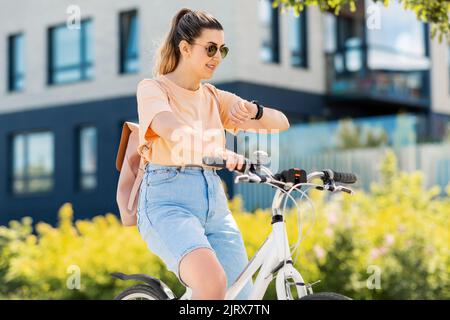 donna con orologio intelligente in bicicletta in città Foto Stock