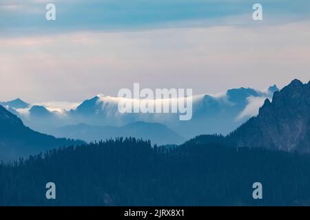 Linea di nuvole basse come una cascata di nuvole che si riversarono sulle creste di Puget Sound, vista da Evergreen Mountain Lookout, Cascade Range, Mt. Baker-Snoq Foto Stock