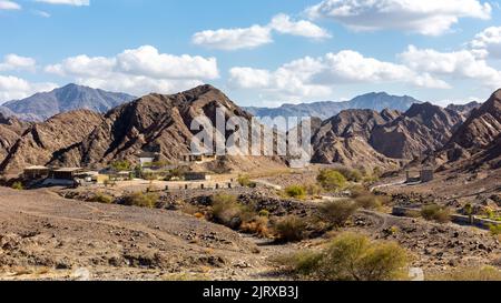 Vista panoramica del letto secco del fiume Wadi Shawka con gli edifici del campo Emirates Adventures, le montagne rocciose Hajar sullo sfondo, Emirati Arabi Uniti. Foto Stock