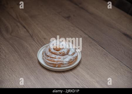 Ciambelle di lumaca su un piatto bianco e sfondo di legno. Dolci alla cannella. Prodotti da forno. Foto Stock