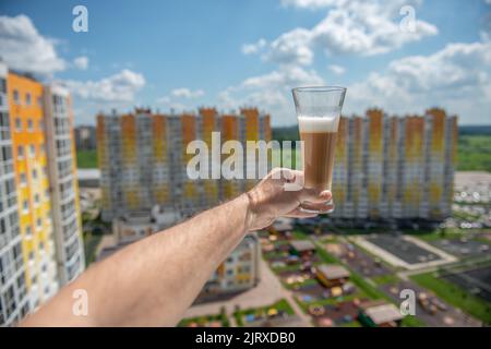 un bicchiere di caffè sulla mano di un uomo si stese nella finestra sullo sfondo di un edificio di appartamenti Foto Stock