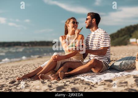 coppia felice con il cibo che ha picnic sulla spiaggia Foto Stock