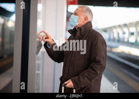 Uomo d'affari senior mascherato in attesa del concetto di mobilità del treno, del covid e del coronavirus Foto Stock