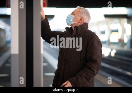 Uomo d'affari senior mascherato in attesa del concetto di mobilità del treno, del covid e del coronavirus Foto Stock