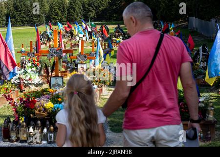 Una famiglia arriva per rispettare le tombe di soldati caduti, uccisi dall'esercito russo durante l'invasione del 2022 nella città vecchia di Lviv al cimitero di Lychakiv, mentre la guerra con la Russia supera i 6 mesi. La città di Lviv ha selezionato una fessura separata di terra al cimitero per i soldati caduti nella lotta con la Russia, i militari sono ampiamente considerati come eroi nazionali. Foto Stock