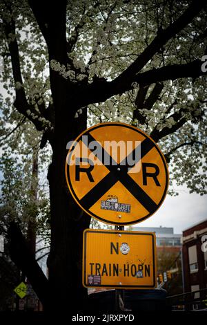 Uno scatto verticale di un cartello di attraversamento ferroviario sotto l'albero Foto Stock