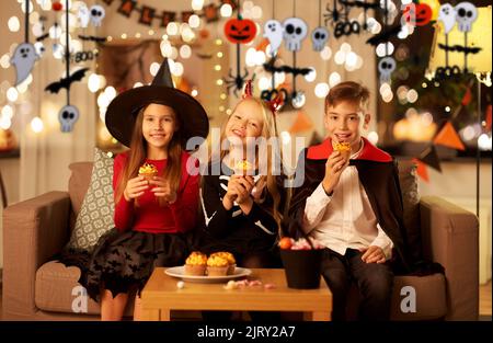 bambini in costumi di halloween mangiare cupcakes a casa Foto Stock