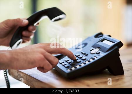 Effettuare la chiamata e farlo avvenire. Un uomo che compone un numero su un telefono al lavoro. Foto Stock