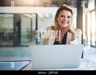 So che Ive ha ottenuto che cosa prende. Ritratto di una giovane donna d'affari sorridente seduta dietro il suo portatile in ufficio. Foto Stock