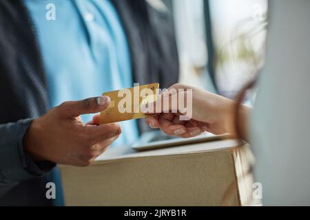 Operare con un servizio di consegna in contanti. Un cliente che utilizza una carta di credito per pagare una consegna effettuata da un corriere. Foto Stock