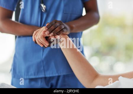 Qui per aiutarvi a raggiungere la strada del recupero. Primo piano di un medico che tiene una mano di un paziente in comodità. Foto Stock