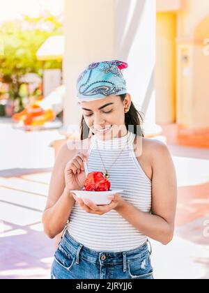 Giovane donna che tiene una tazza di ghiaccio rasato sulla strada. Concetto di una ragazza con un raspado Nicaraguano. Ritratto di ragazza sorridente che tiene il ghiaccio rasato dentro Foto Stock