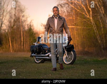 L'uomo di mezza età in giacca di pelle si allontana eroicamente dalla moto, Karlsruhe, Germania Foto Stock