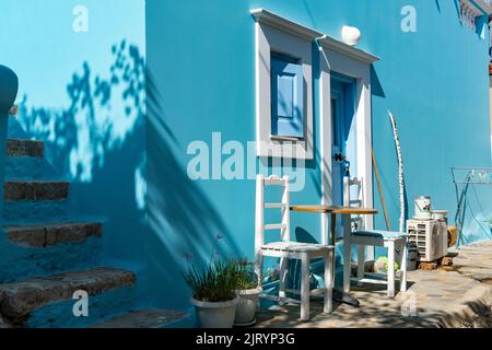 Tradizionale casa greca con facciata blu con porta e finestra ad arco bianche e fronte con sedie bianche e tavolo Foto Stock
