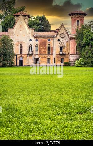 ITALIA, MIRADOLO - CIRCA AGOSTO 2020: Castello di design gotico situato in un giardino all'italiana, pieno di mistero, con luce del tramonto. Foto Stock