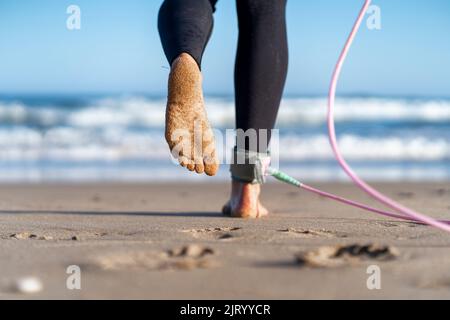 Il surfista che cammina sulla spiaggia si affola con la tavola da surf la mattina. Donna surfista femminile Foto Stock