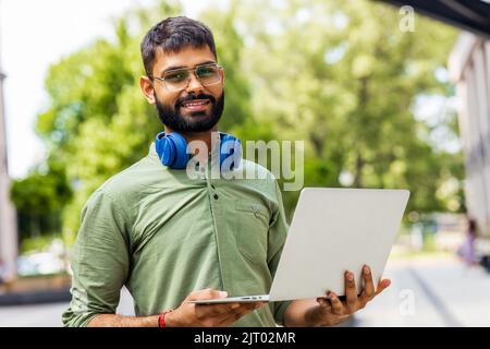 Ritratto studente indiano programmatore utilizzando computer portatile in parco Foto Stock