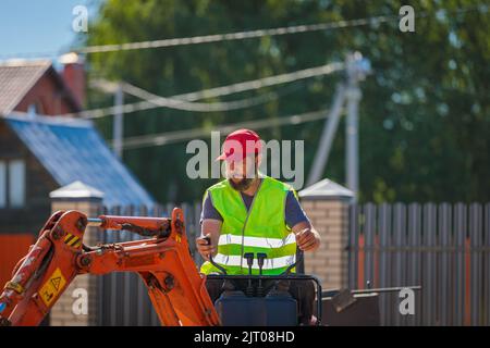 Un uomo su un miniescavatore livella un pezzo di terra, allenta il terreno Foto Stock