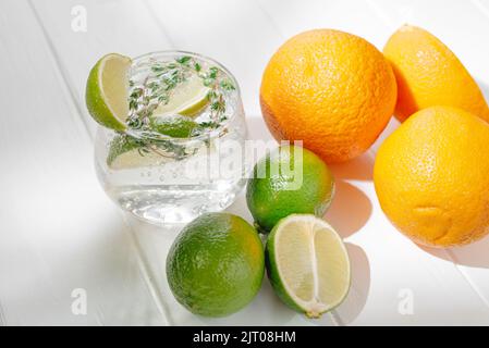 Cocktail alcolico in bicchiere su fondo chiaro con lime e timo e arancia Foto Stock