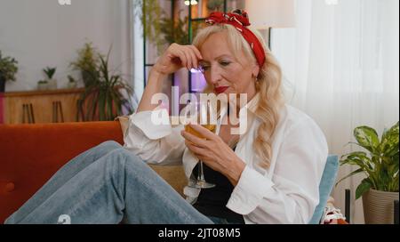Triste nonna anziana donna seduta a casa sembra penoso soffre di situazione sleale, malattie, disperazione bere champagne. Problema, rottura, sensazione di depressione male infastidito, burnout, fallimento Foto Stock