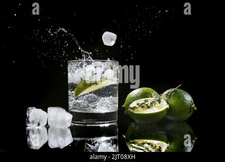 seltzer duro con calce su fondo di legno scuro, cubetti di ghiaccio cadono in un bicchiere con una bevanda alcolica seltzer duro spruzzi di bevanda. Foto Stock