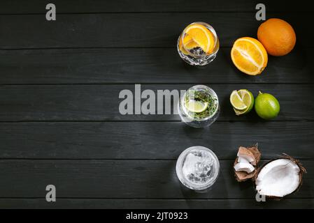 Set di diversi cocktail di seltzer duro su uno sfondo di legno nero. Vista dall'alto. Cocktail con lime arancio e cocco. Tre bevande fredde Foto Stock