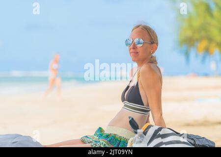 donna bionda che si rilassa sulla spiaggia tropicale con occhiali da sole in bikini Foto Stock