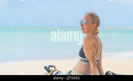 donna bionda che si rilassa sulla spiaggia tropicale con occhiali da sole in bikini Foto Stock