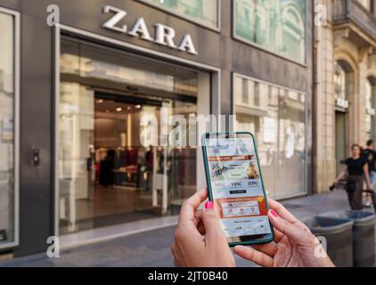 Donna che tiene uno smartphone con l'app Shin sullo schermo e un negozio Zara sullo sfondo Foto Stock