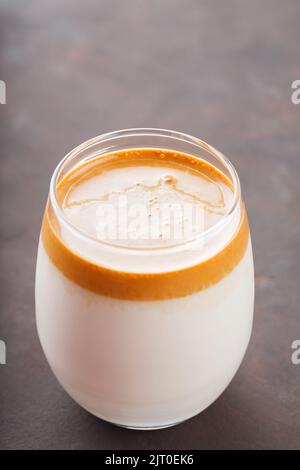 Caffè Dalgona freddo coreano in vetro su sfondo scuro. Caffè Dalgona in un primo piano in vetro trasparente. Nuova tendenza popolare delle bevande Foto Stock