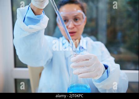 Attenzione alla pipetta da laboratorio nelle mani di scienziato sfocato, farmacologo, ricercatore clinico che pipettano il liquido blu Foto Stock