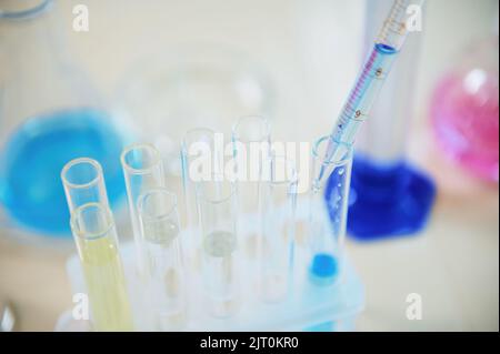 Concentrarsi sul gocciolamento del reagente da una pipetta di vetro da laboratorio in una provetta con sostanza chimica liquida blu in laboratorio Foto Stock