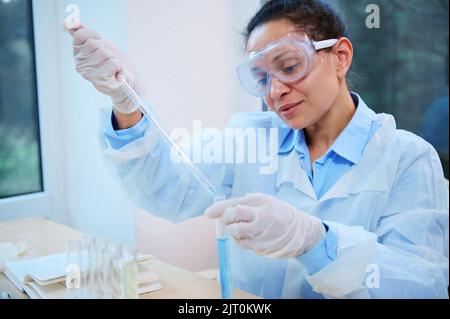 Il farmacologo latino-americano utilizza una pipetta graduata in vetro, gocciola una sostanza in una provetta in laboratorio scientifico Foto Stock