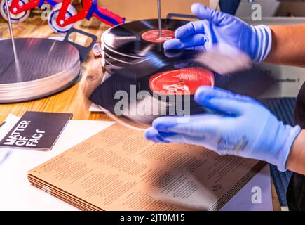 22 agosto 2022, Meclemburgo-Pomerania occidentale, Güstrow: I dipendenti della società discografica 'questione di fatto' controllano e imballano i record appena pressati nelle loro copertine. (L'azienda, che attualmente impiega cinque persone, produce record per diverse settimane in un ex locale per la patata, che ha dovuto essere ampiamente convertito per la produzione da record. Con una forza di 150 tonnellate, le lunghe registrazioni sono prodotte da cloruro di polivinile (PVC) sulle presse a 200 gradi Celsius. Ogni anno devono essere premuti tra 250.000 e 300.000 record. Secondo l'Associazione tedesca dell'industria musicale, Foto Stock