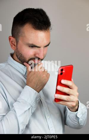 Bell'uomo caucasico che tiene il telefono rosso e guarda qualcosa con curiosità Foto Stock