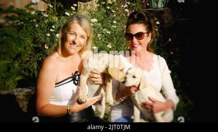 Due femmine attraenti che reggono un paio di cuccioli labrador - John Gollop Foto Stock