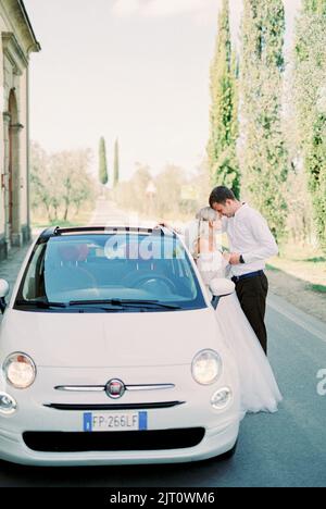 Milano, Italia - 07.04.21: Sposa e sposo sono in piedi sulla strada asfaltata accanto alla vettura Fiat 500 Foto Stock