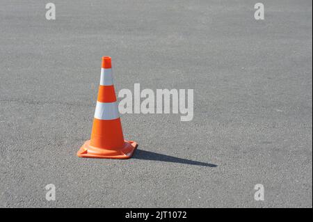 cono stradale, con strisce bianche e arancioni su asfalto grigio, spazio copia. Bel tempo Foto Stock