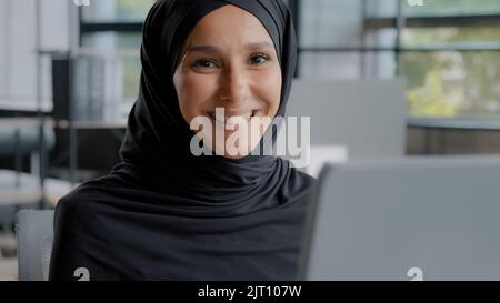 Primo piano positivo giovane donna ufficio lavoratore professionale manager che lavora al computer attraente successo arabo businesswoman in hijab seduta a. Foto Stock