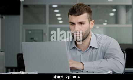 Un dirigente d'affari serio e focalizzato che lavora su un computer portatile che comunica con un collega tramite videochiamata discutendo di piano di lavoro responsabile professionale dell'ufficio Foto Stock