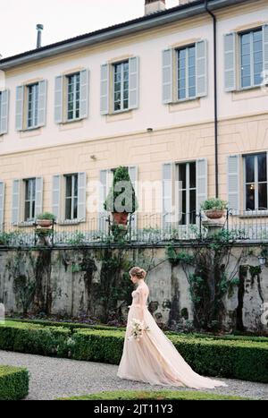 La sposa cammina lungo un sentiero di ghiaia nel parco, passando per una vecchia villa. Como, Italia Foto Stock