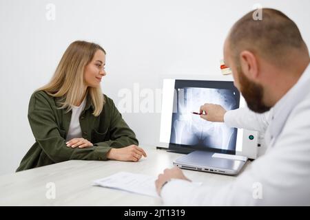 Medico ortopedico che mostra l'immagine radiografica alla sua paziente femmina durante la consultazione in clinica Foto Stock