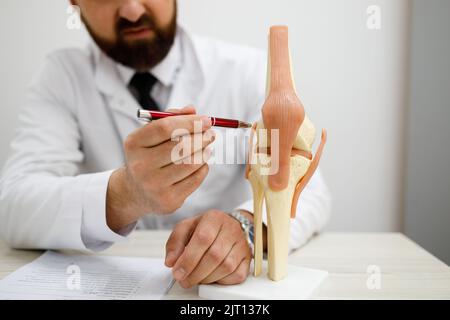 Il medico maschile mostra modello di articolazione artificiale del ginocchio umano in ufficio medico Foto Stock