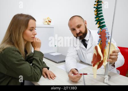 Medico maschile che spiega il modello della colonna vertebrale a un paziente giovane Foto Stock