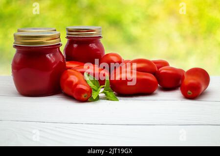 Tradizionale salsa di pomodoro italiana in un vasetto di vetro con pomodori freschi e basilico. Spazio di copia. Foto Stock