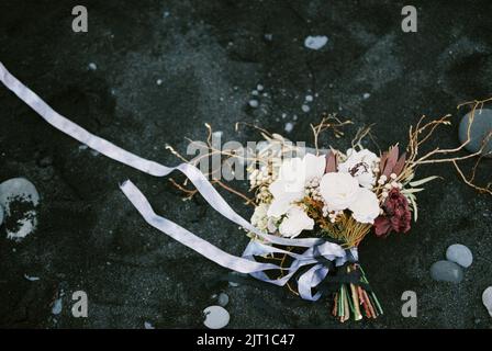 Il bouquet di nozze con un nastro blu si trova sulla sabbia nera. Vista dall'alto Foto Stock