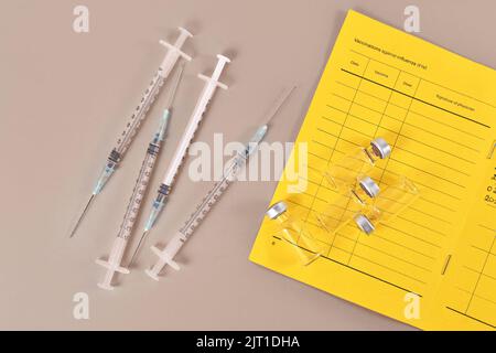 Concetto per la vaccinazione di richiamo del virus Corona che mostra il passaporto del vaccino con 4 siringhe e flaconcini Foto Stock