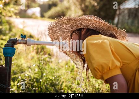 la ragazza carina beve acqua da una colonna fuori in estate Foto Stock