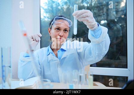 Donna ispanica assistente di laboratorio esperto esamina il liquido in provette, controlla i test. Il farmacologo lavora in laboratorio Foto Stock